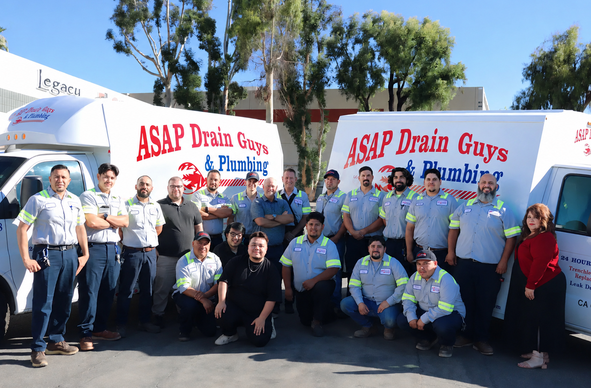 A group of plumbers and staff pose in front of two ASAP Drain Guys & Plumbing service vans, ready to tackle plumbing repair and general plumbing needs, on a sunny day in the parking lot.